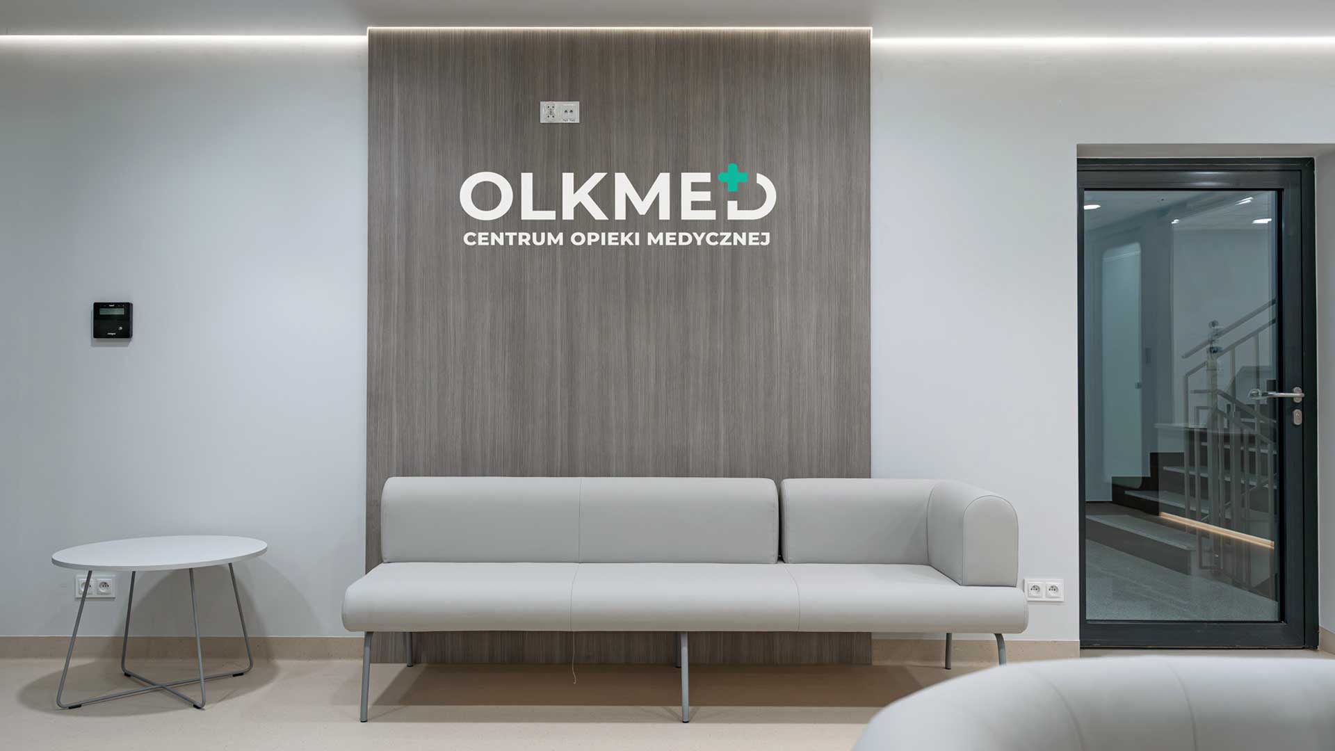 Nowoczesne wnętrze recepcji centrum medycznego OLKMED z minimalistycznym wystrojem i wygodną kanapą.
