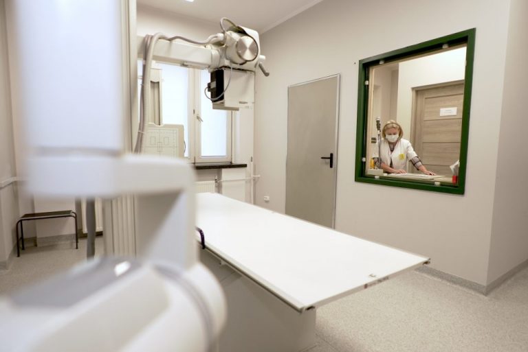 Nowoczesne wnętrze gabinetu radiologicznego z widoczną aparaturą i pracownikiem w maseczce.